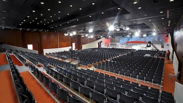 Un auditorio amplio con filas de sillas negras, un escenario con equipo de iluminación y una alfombra roja.