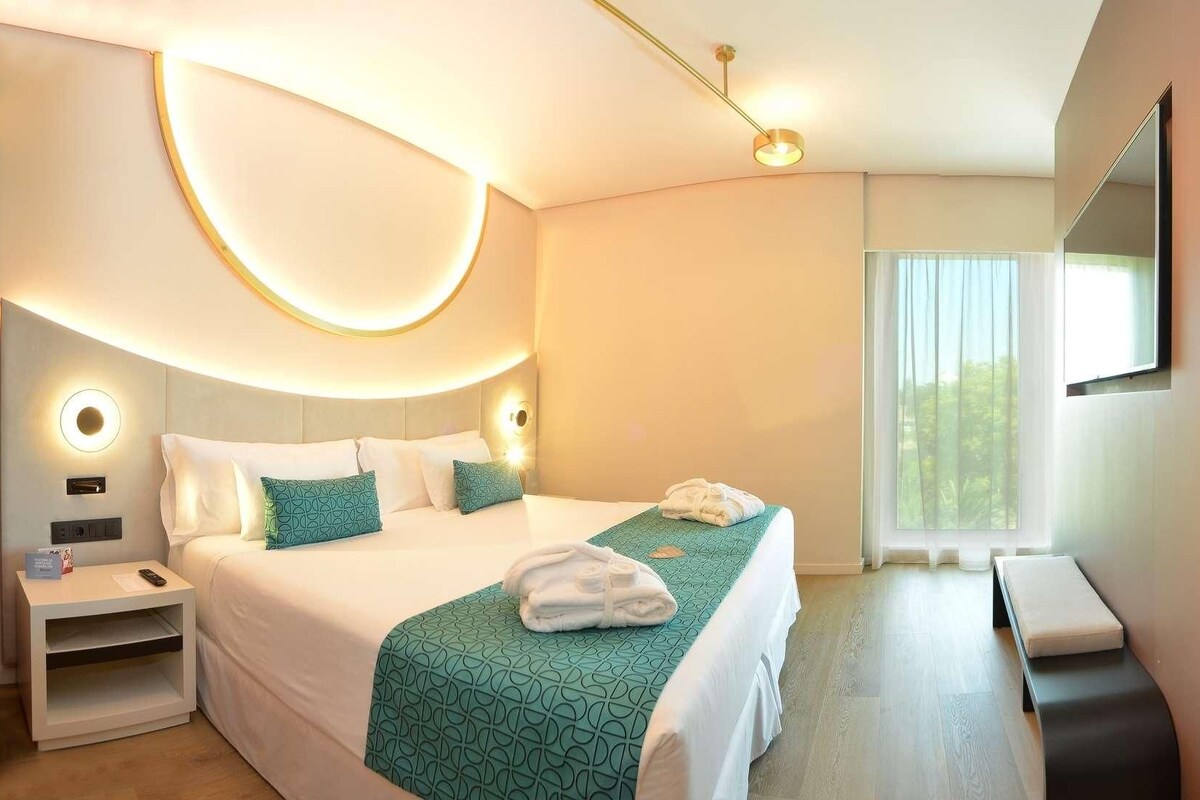 A modern hotel room with a bed, bedside table, and a seating area with a sofa and a small table.