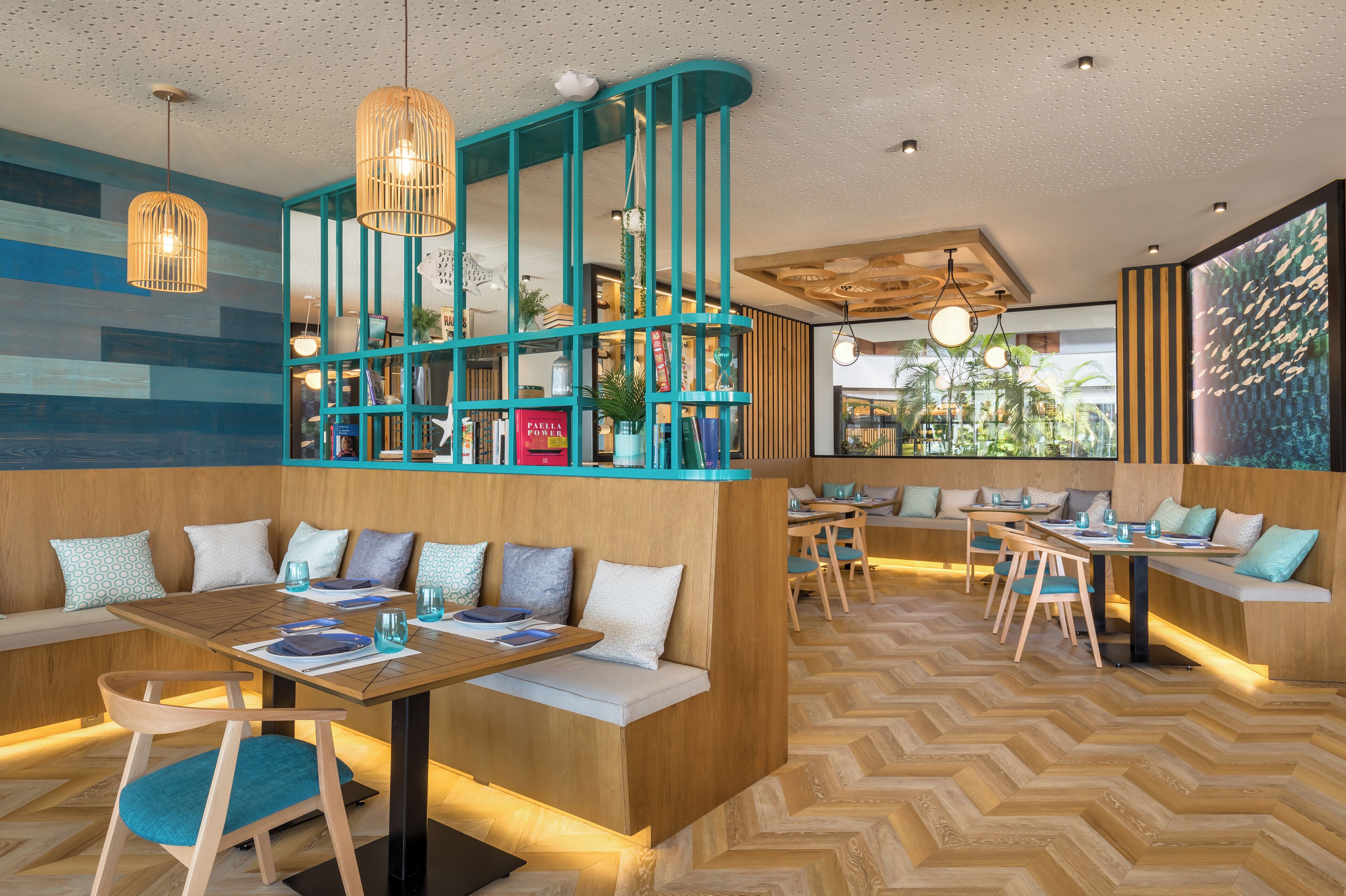 Un restaurante moderno con detalles en madera y tonos turquesa, que cuenta con zonas de estar con bancos y mesas, y un suelo con estampado de espiga.