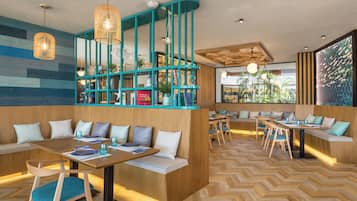 Un restaurante moderno con detalles en madera y tonos turquesa, que cuenta con zonas de estar con bancos y mesas, y un suelo con estampado de espiga.