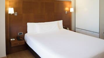 A neatly made bed with white linens, a wooden headboard, bedside lamps, and a nightstand with a phone and a tissue box.