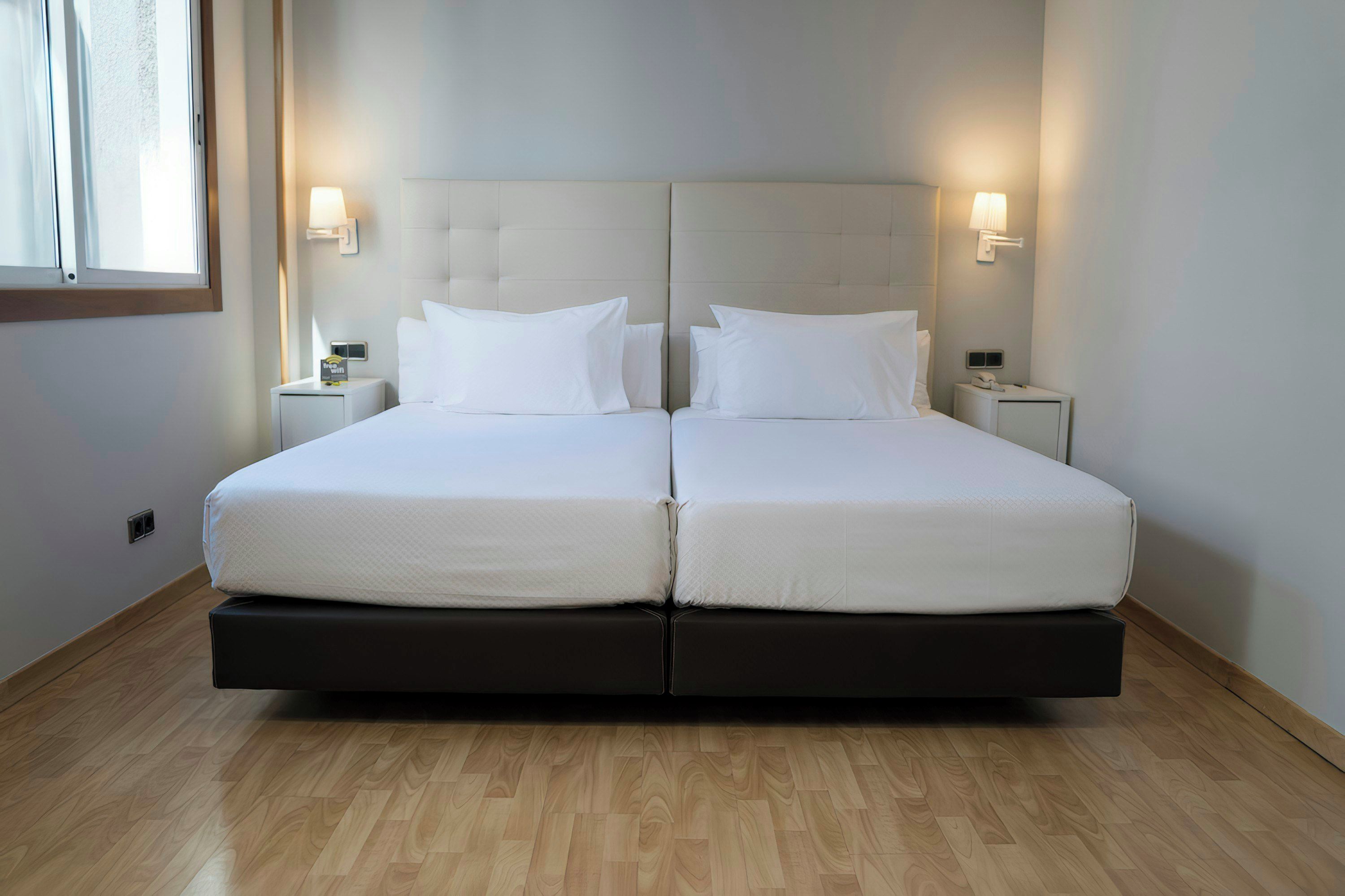 A double bed with a padded headboard, two bedside tables with lamps, and a window with curtains.