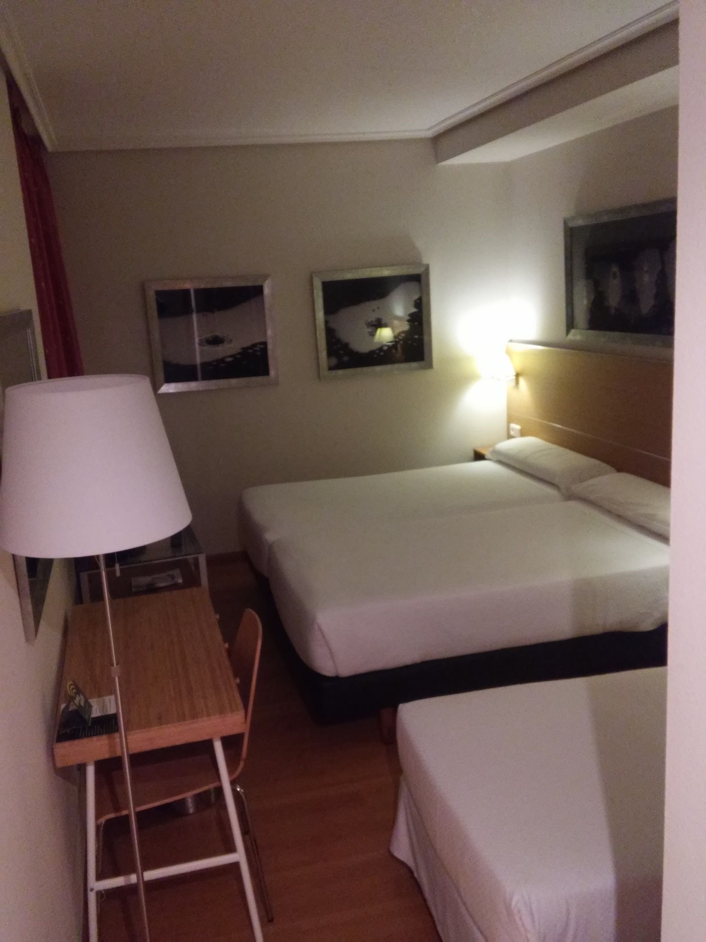 A hotel room with a desk, two beds, a chair, and a ladder.
