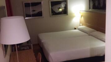 A hotel room with a desk, two beds, a chair, and a ladder.