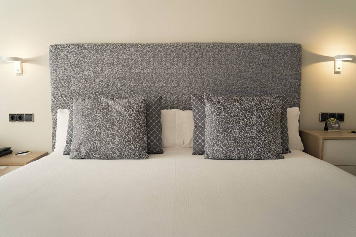 A hotel room with a large bed, grey patterned headboard, and two bedside tables with lamps.
