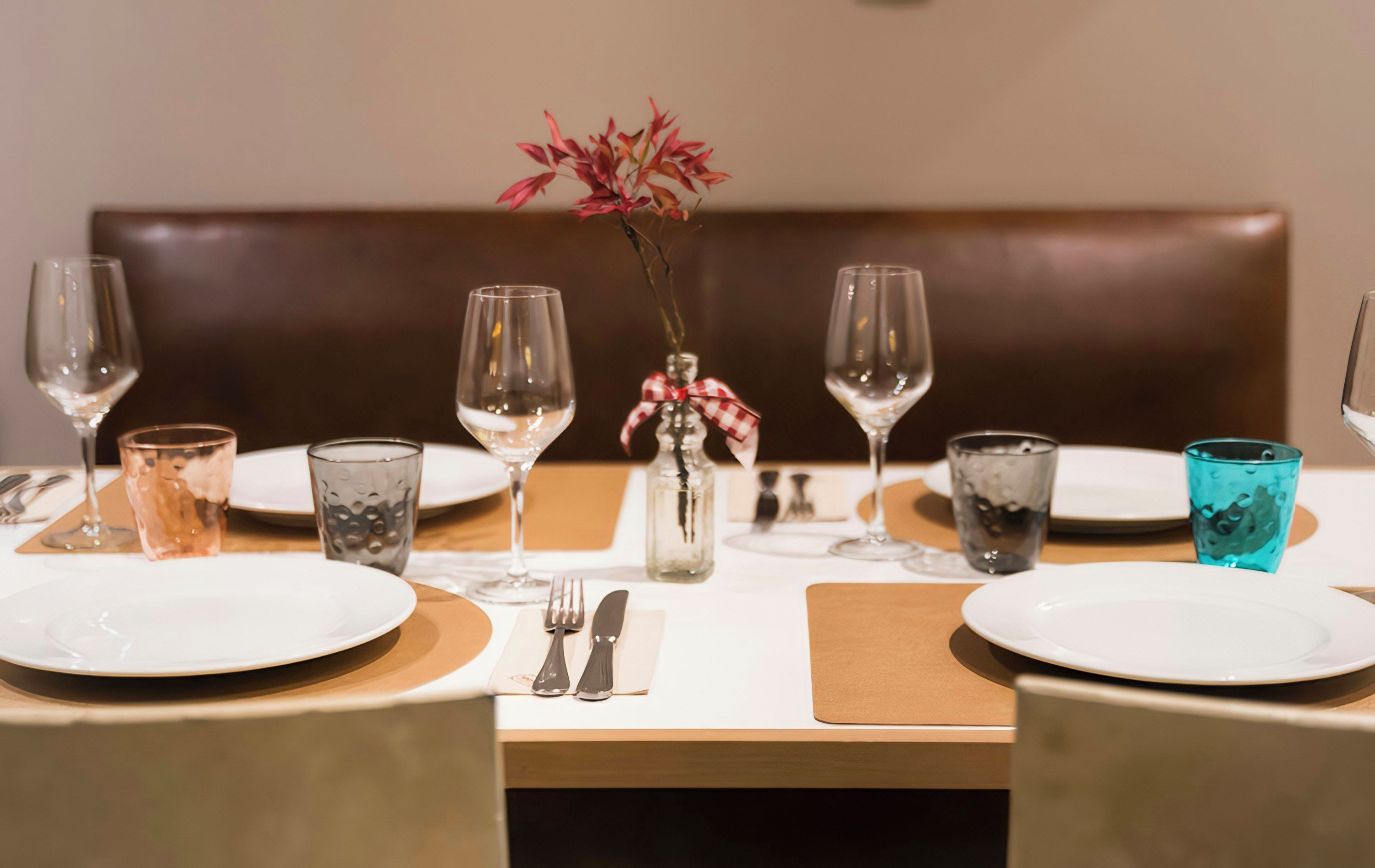 Una mesa de comedor dispuesta con platos, cubiertos y vasos, con un florero en el centro.