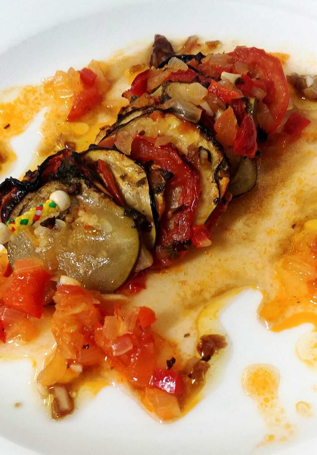 Un plato con berenjena en rodajas, tomates y salsa cremosa.