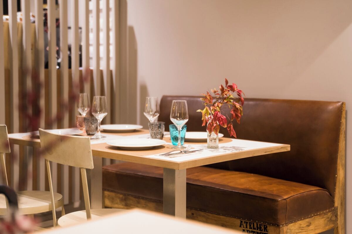 Een eettafel gedekt met borden, glazen en een vaas met rode bladeren.