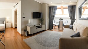A modern living room with a sofa, a TV, a dining table with chairs, and a small kitchen area. - Hotel Sercotel Tres Luces (Vigo)