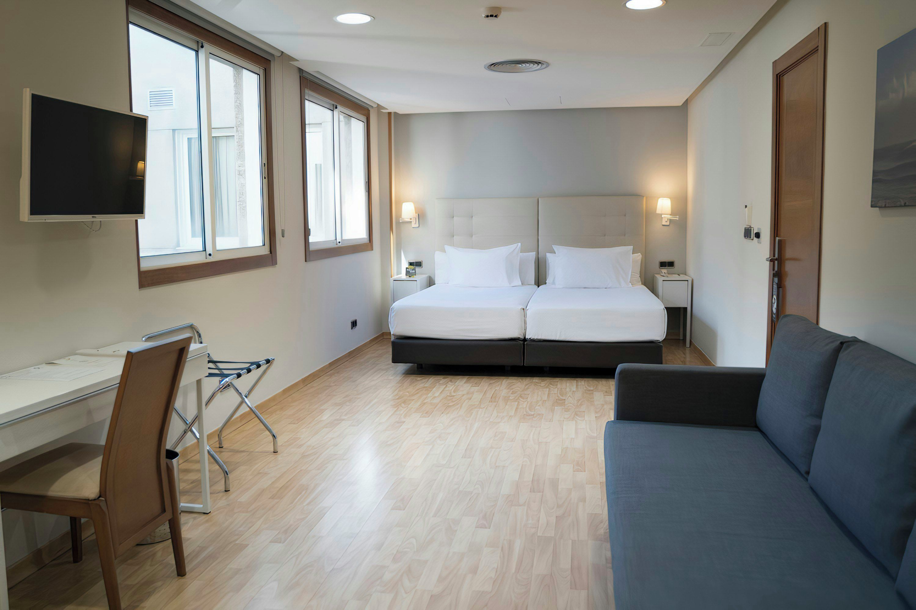 A hotel room with a bed, a desk, a chair, a sofa, and a TV.