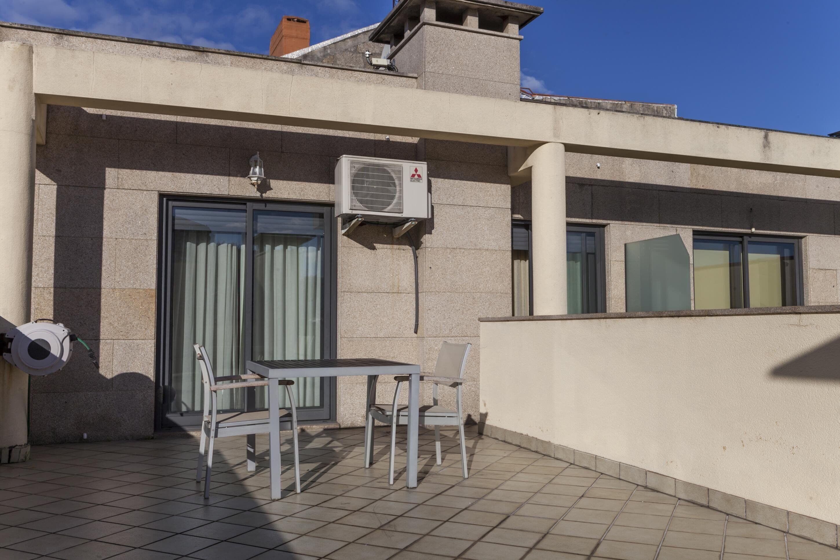 Un balcón con una mesa y sillas, un equipo de aire acondicionado y una puerta con cortinas.
