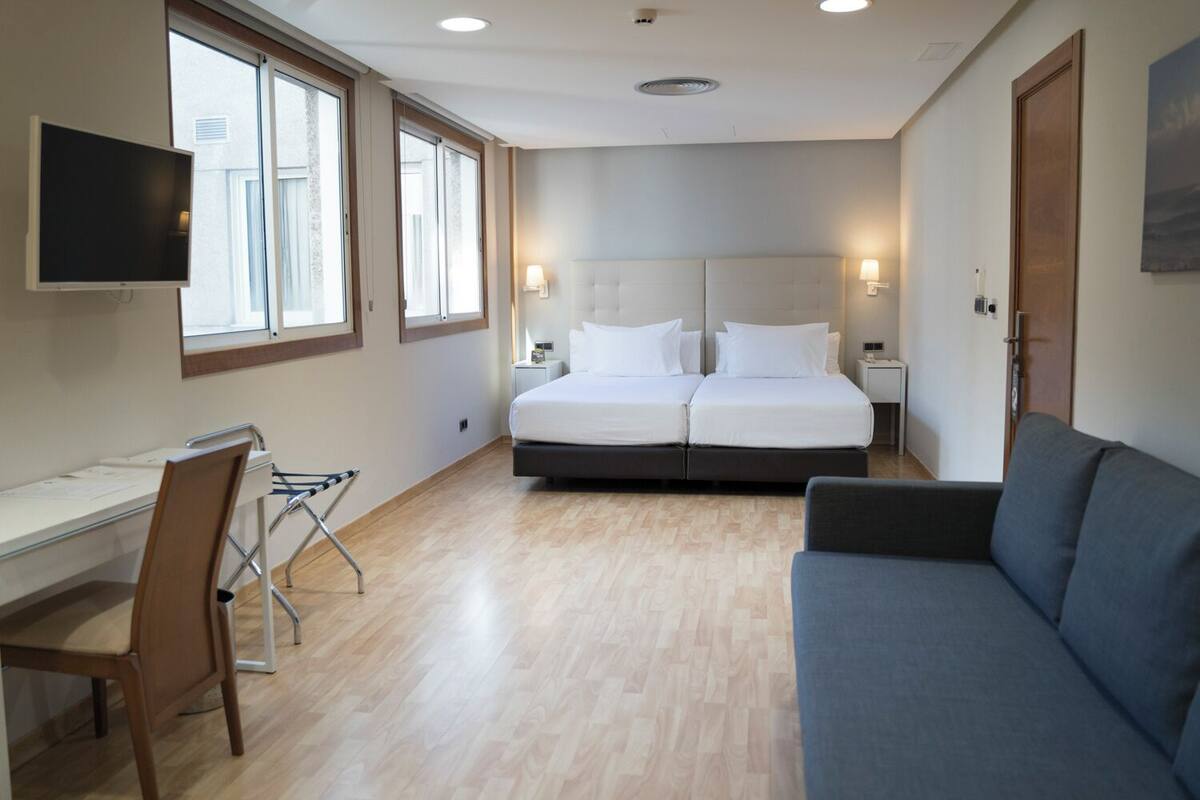 A hotel room with a bed, a desk, a chair, a couch, and a TV.