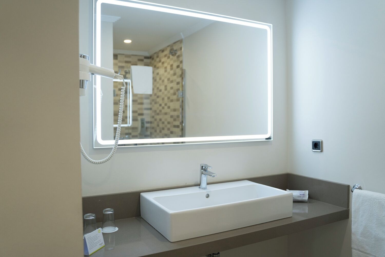 Une salle de bain moderne avec un grand miroir, un lavabo blanc et un porte-serviettes.