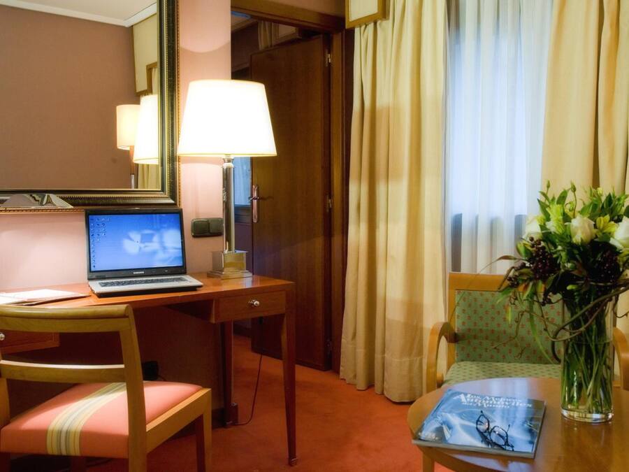 A hotel room with a desk, laptop, chair, and a vase with flowers.