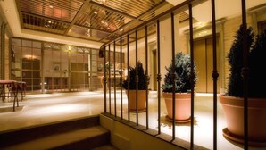 A spacious indoor area with a staircase leading to a lower level, large potted plants, and a modern ceiling design. - Hotel Palafox (Zaragoza)