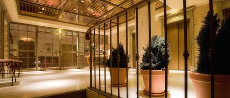 Un espacio interior amplio con una escalera que baja a un nivel inferior, grandes plantas en macetas y un diseño de techo moderno.