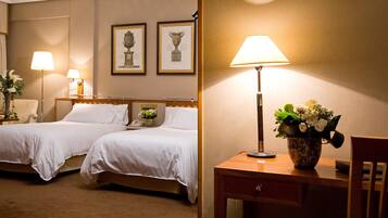 A hotel room with two beds, a desk with a lamp, and a vase of flowers.