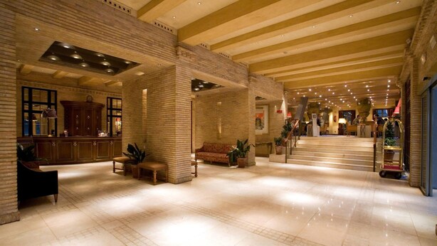 A spacious lobby with a high ceiling, a reception area, and a staircase leading to upper floors. - Hotel Palafox (Zaragoza)
