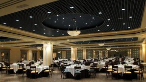 A large banquet hall with round tables set for dining, high ceilings with a grid pattern, and large chandeliers. - Hotel Palafox (Zaragoza)