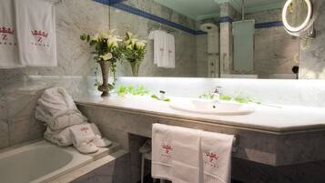 Baño con encimera de mármol, bañera, lavabo y espejo. Hay toallas colgadas en la pared y un jarrón con flores sobre la encimera.
