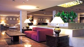 A lobby with a reception desk, a sofa, a coffee table, and a lamp. - Hotel Goya (Zaragoza)