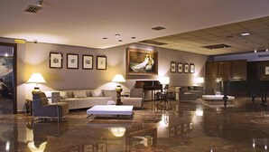 A spacious lobby with a marble floor, a sofa set, a piano, and framed artwork on the walls. - Hotel Goya (Zaragoza)