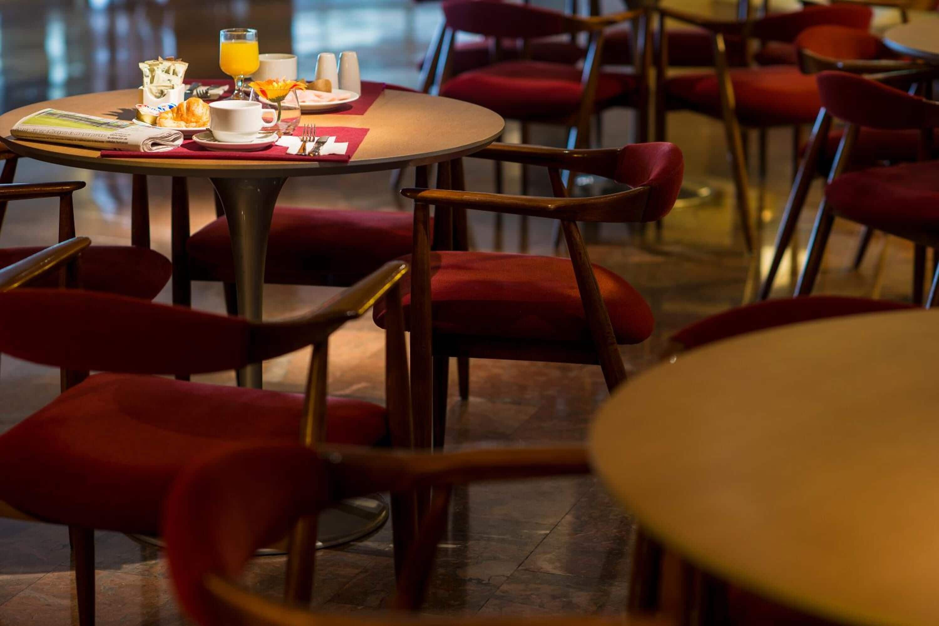 A dining area with round tables and red upholstered chairs.