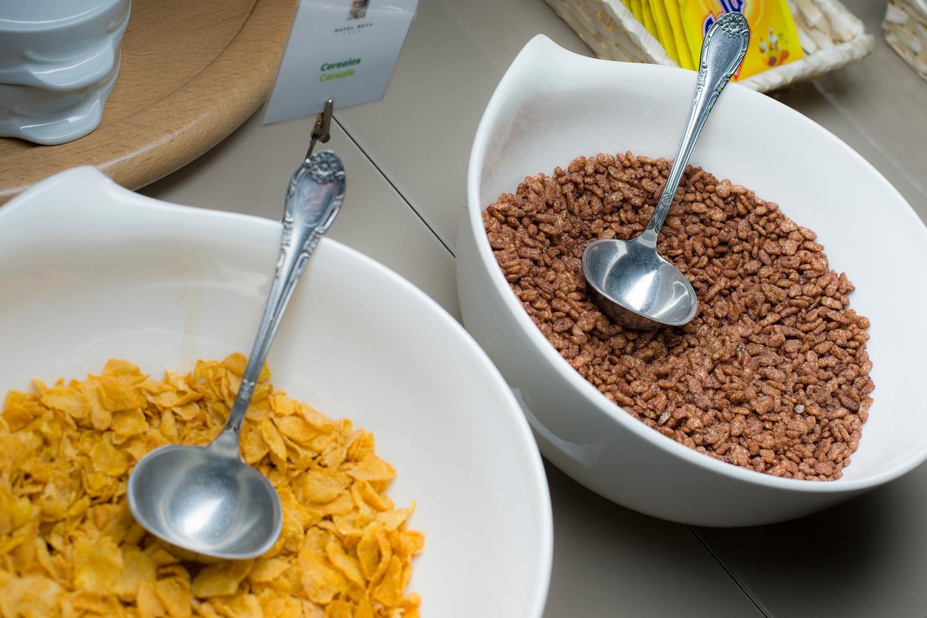 Dos tazones blancos llenos de diferentes tipos de cereal, cada uno con una cuchara.