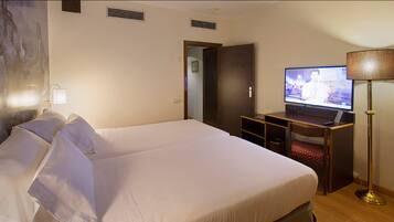 Habitación de hotel con una cama grande, un escritorio con una computadora portátil, un televisor y una lámpara de pie.