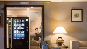 A lobby with a vending machine, a lamp, and two chairs. - Hotel Goya (Zaragoza)