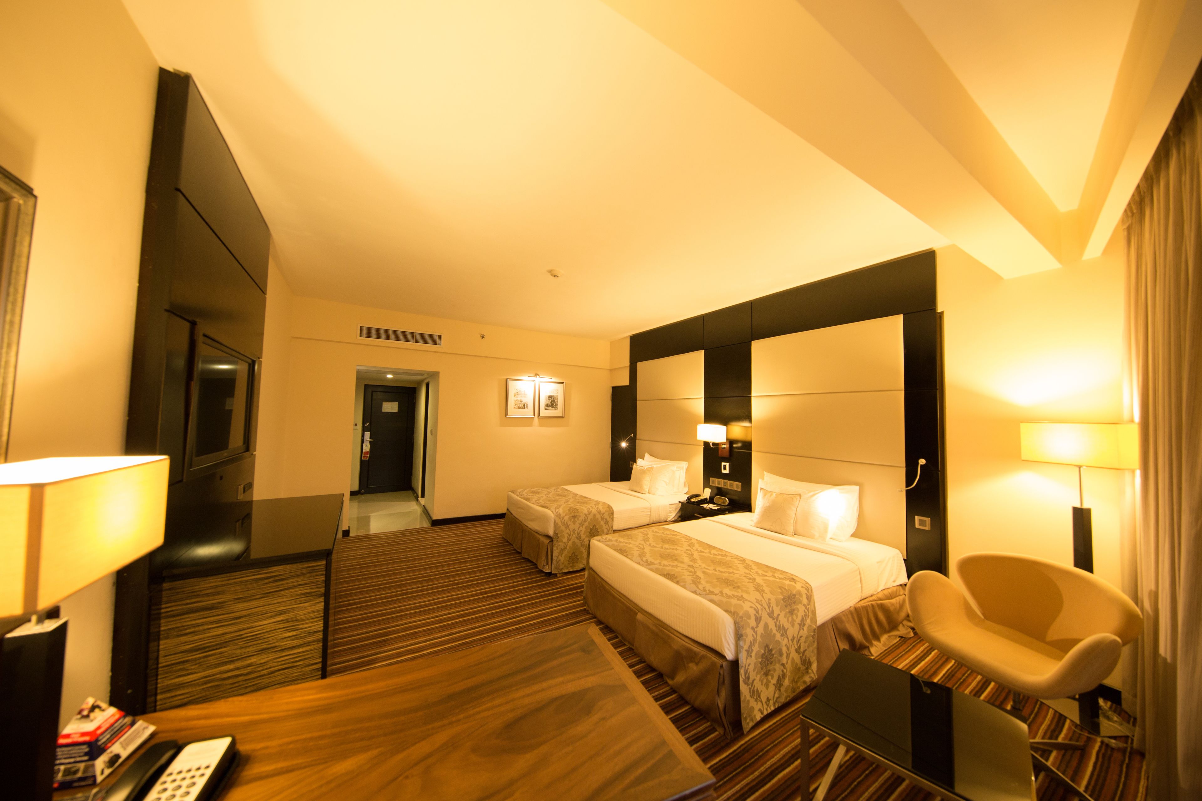 A hotel room with two beds, a desk, a chair, and a desk lamp.