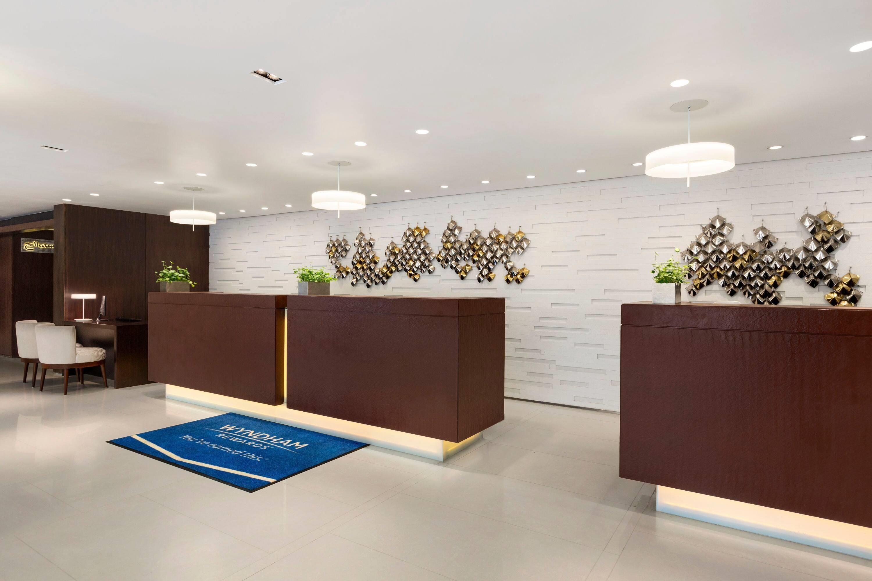 A modern reception area with a reception desk, a blue carpet with text, and a wall-mounted decorative piece.