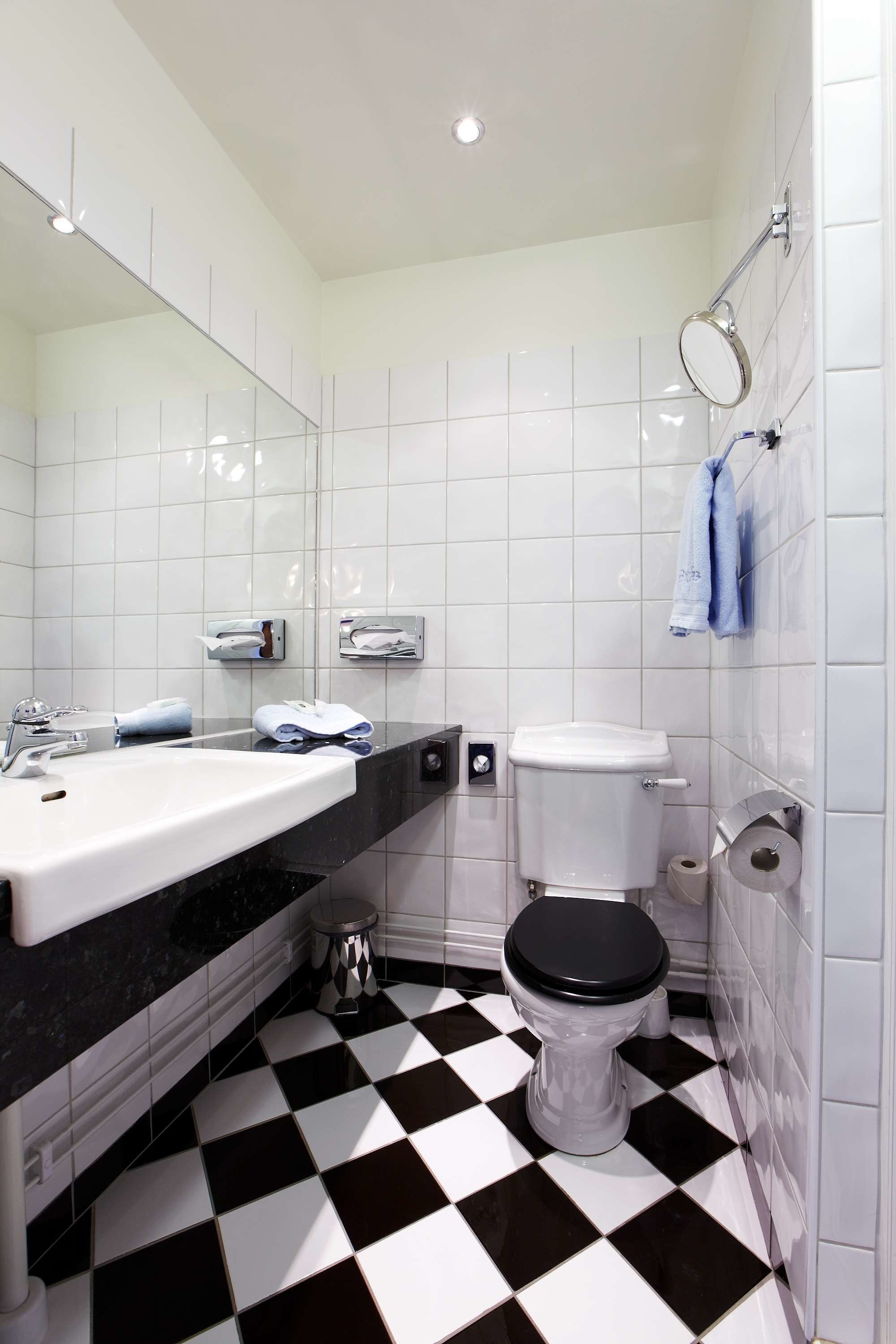 Un baño con piso a cuadros blanco y negro, un lavamanos blanco y un inodoro.