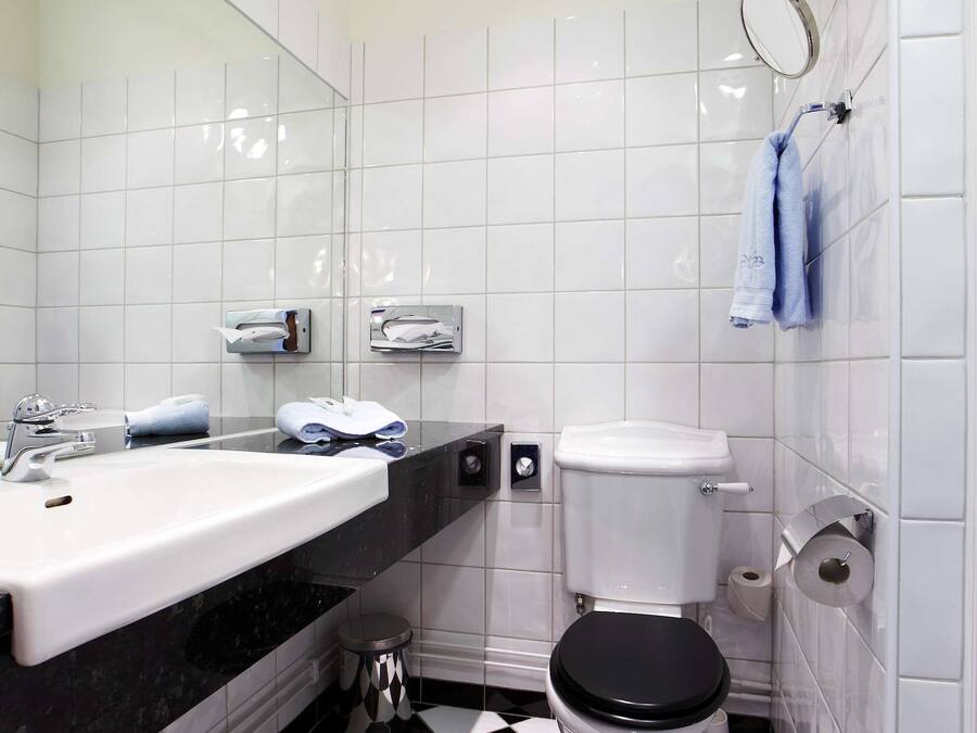 Un baño con piso a cuadros blanco y negro, un lavamanos blanco y un inodoro.