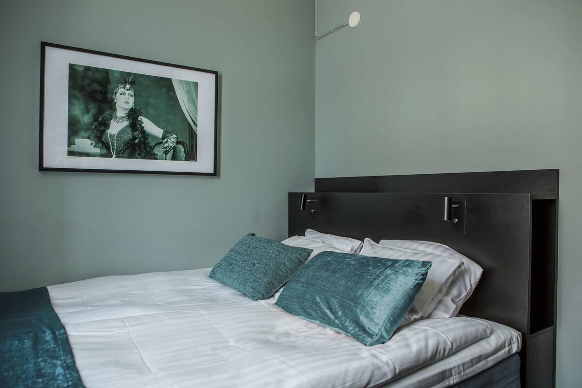 A neatly made bed with white linens and teal pillows, a framed picture on the wall, and a modern headboard.