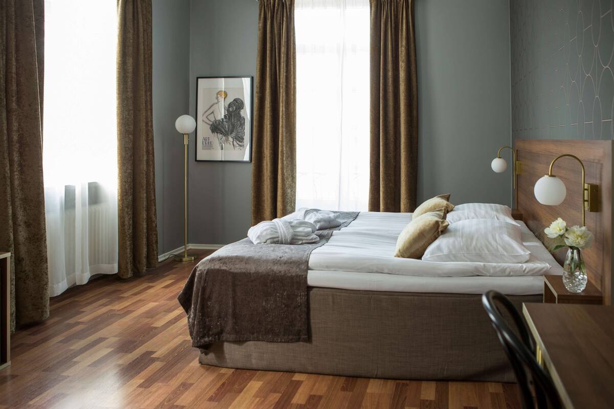 A neatly made bed with a blanket and pillows, a bedside table with a vase of flowers, and a floor lamp.