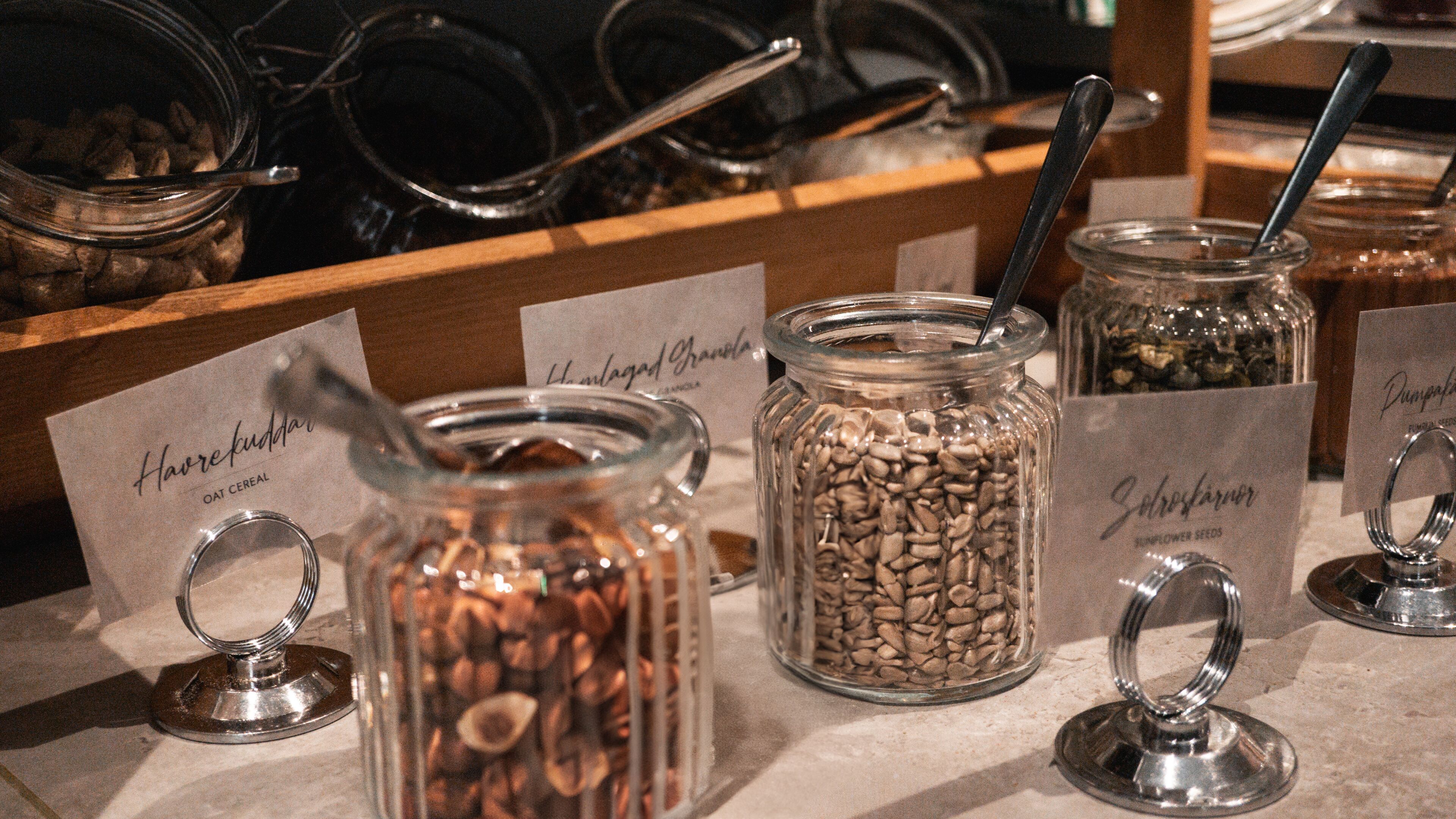 A breakfast bar with labeled jars of granola, oats, and sunflower seeds.