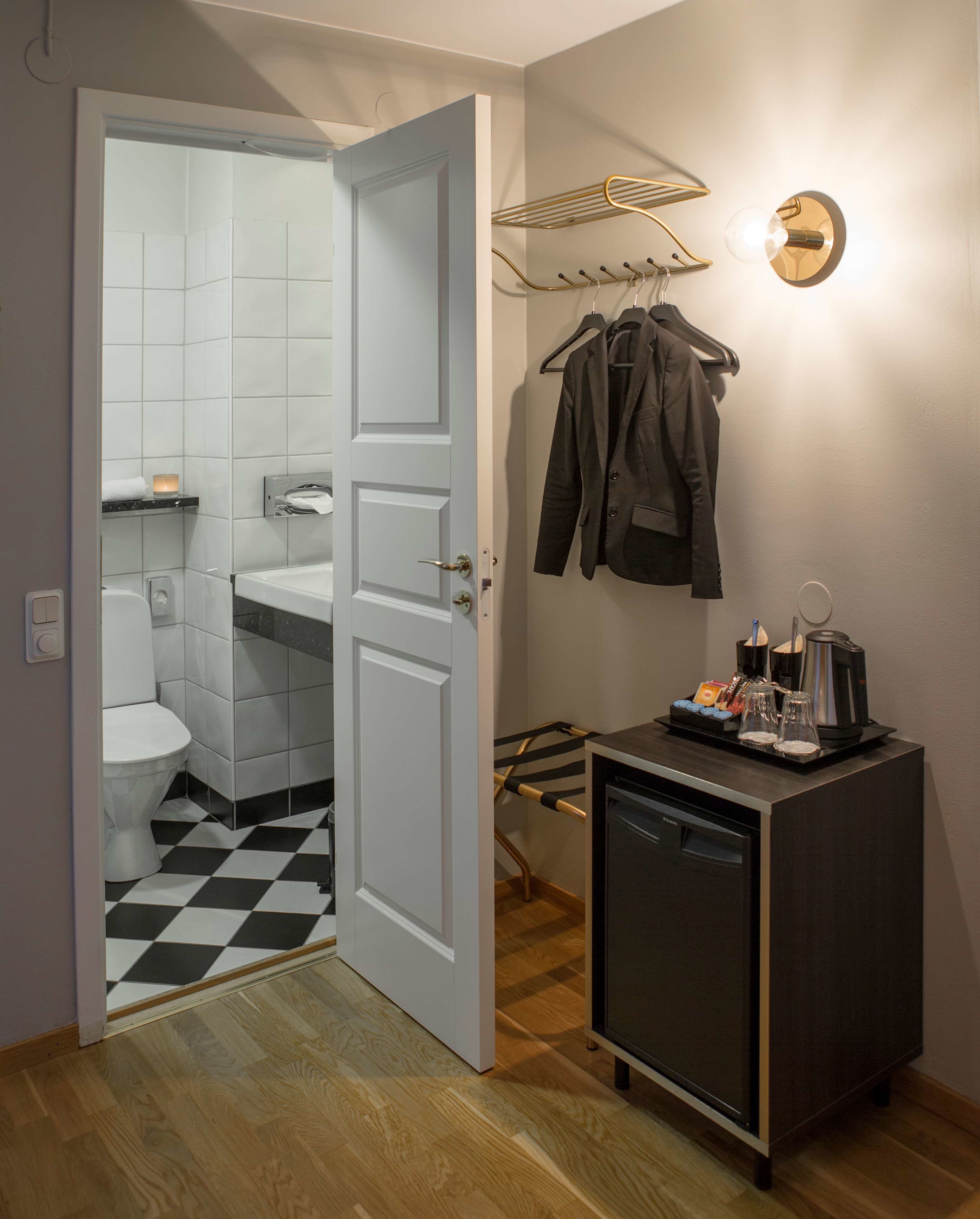 Habitación de hotel compacta con baño, una kitchenette pequeña y un perchero con chaquetas.