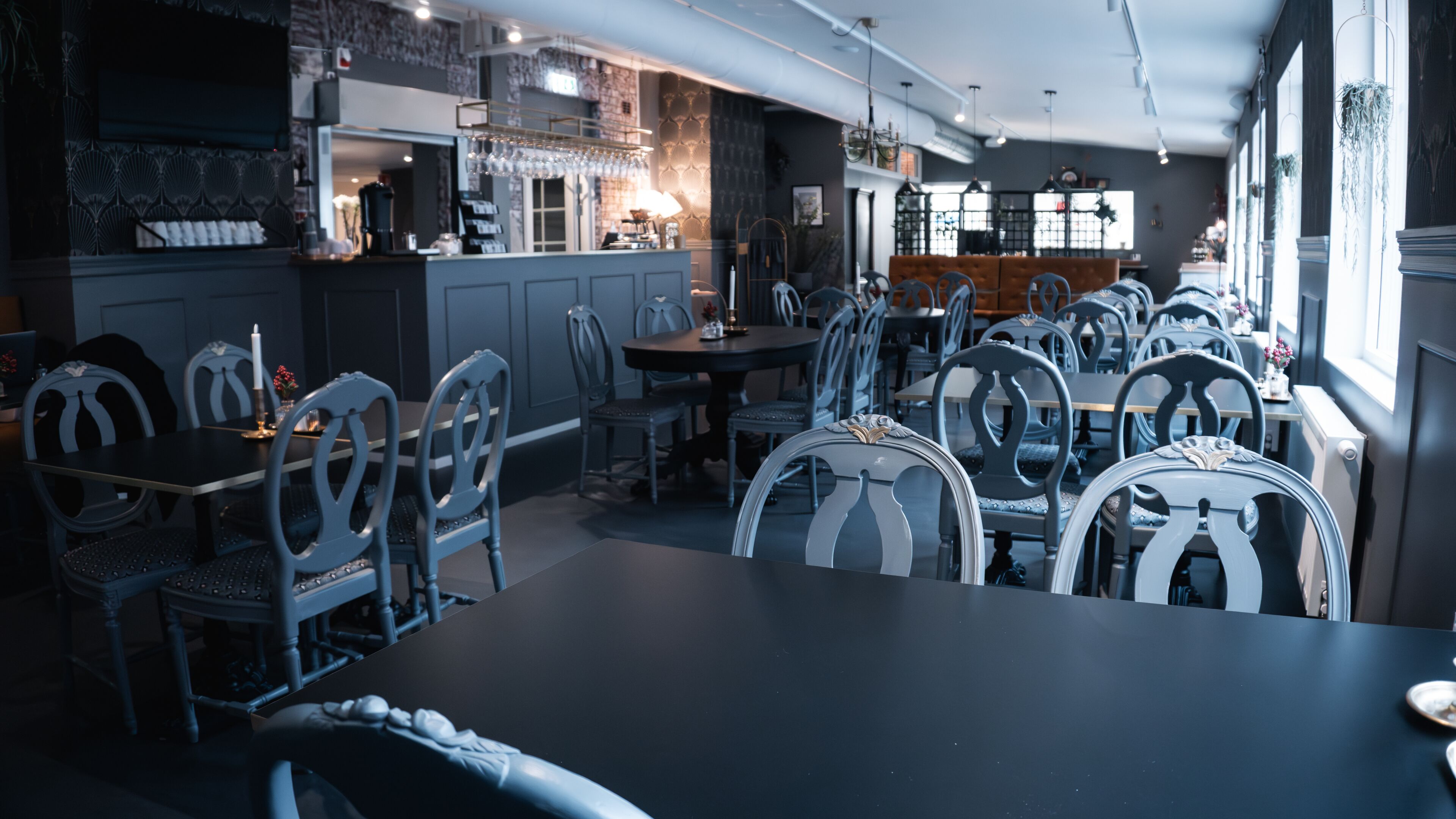 A restaurant with multiple tables and chairs, a bar area, and a counter with a coffee machine.