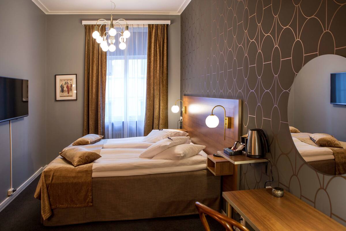 A hotel room with a large bed, a desk with a chair, a flat-screen TV, a coffee maker, and a window with curtains.