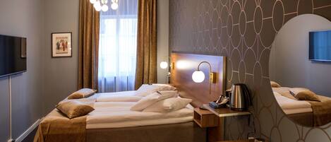 Habitación de hotel con una cama grande, un escritorio con silla, televisor de pantalla plana, cafetera y ventana con cortinas.