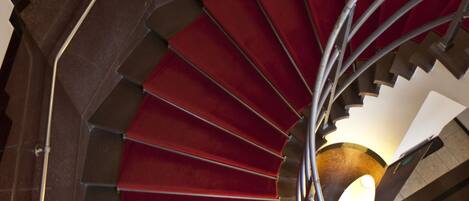 Una escalera de caracol con peldaños alfombrados de rojo y barandilla de metal.