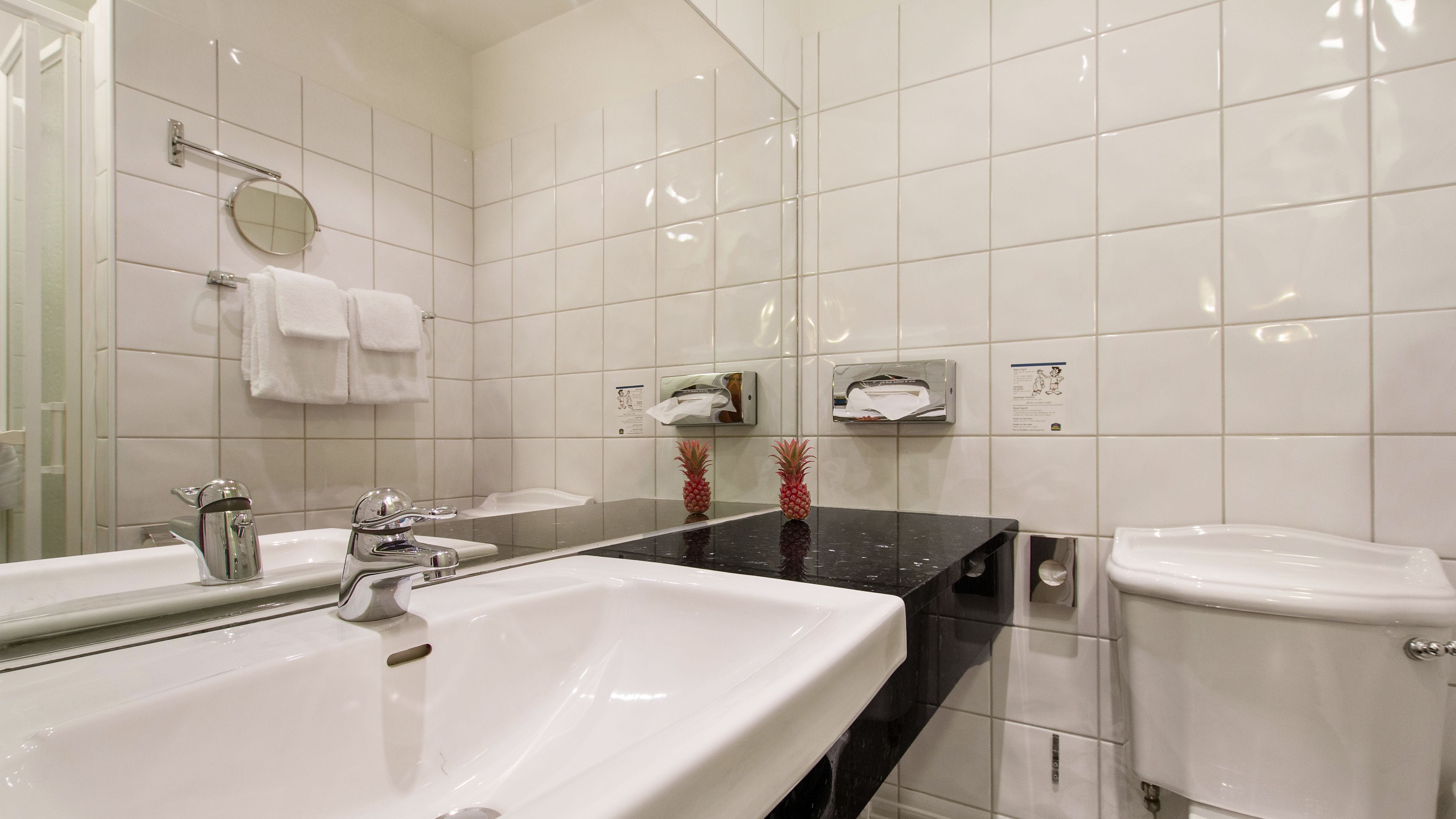 Un baño con azulejos blancos, un lavabo, un inodoro y un espejo.