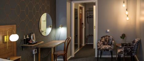 A hotel room with a bed, a desk, a chair, a mirror, and a hanging light fixture.