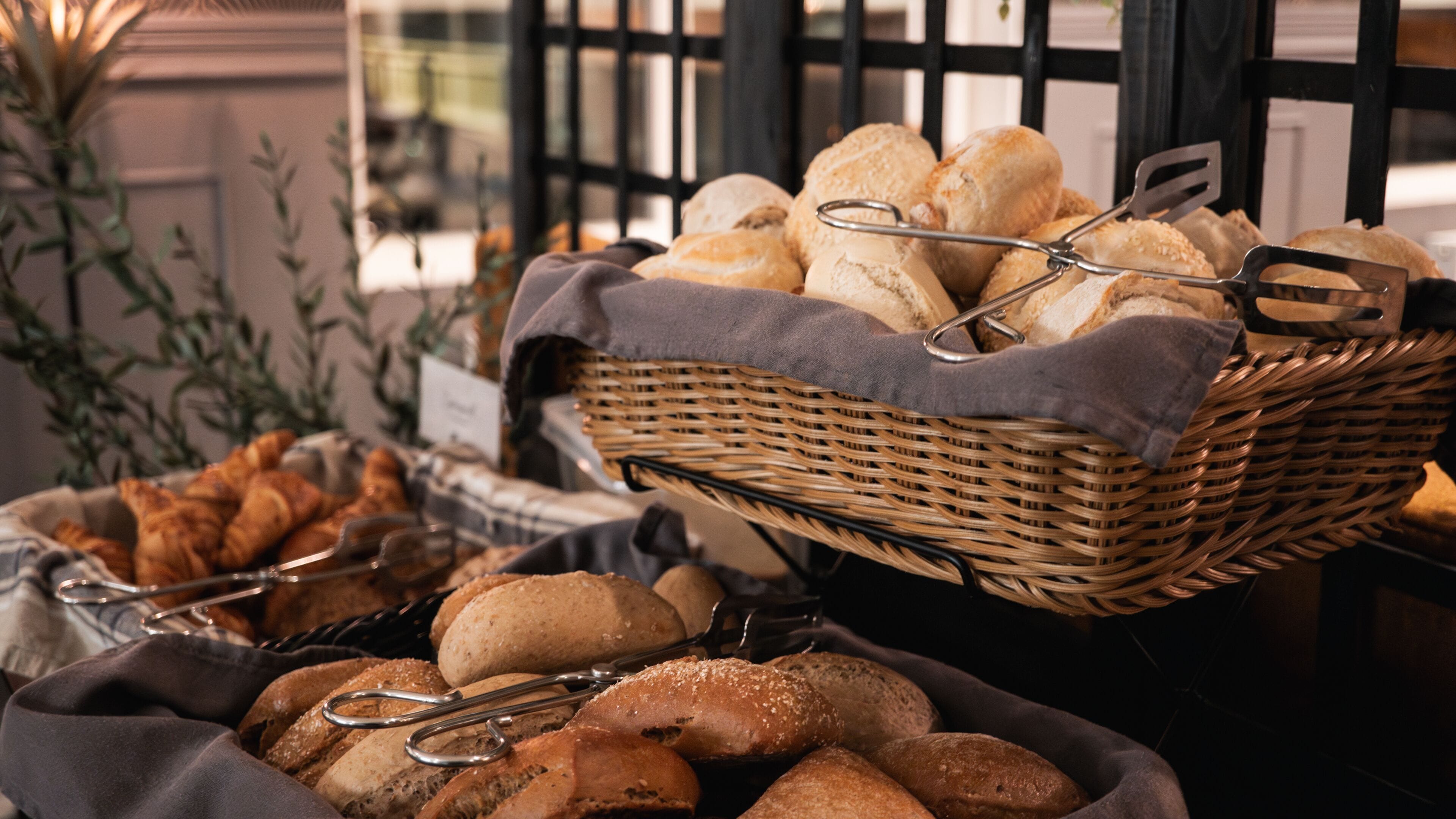 Une table de buffet proposant une variété de pains et de viennoiseries, notamment des croissants et des baguettes, présentés dans des paniers et sur une nappe.