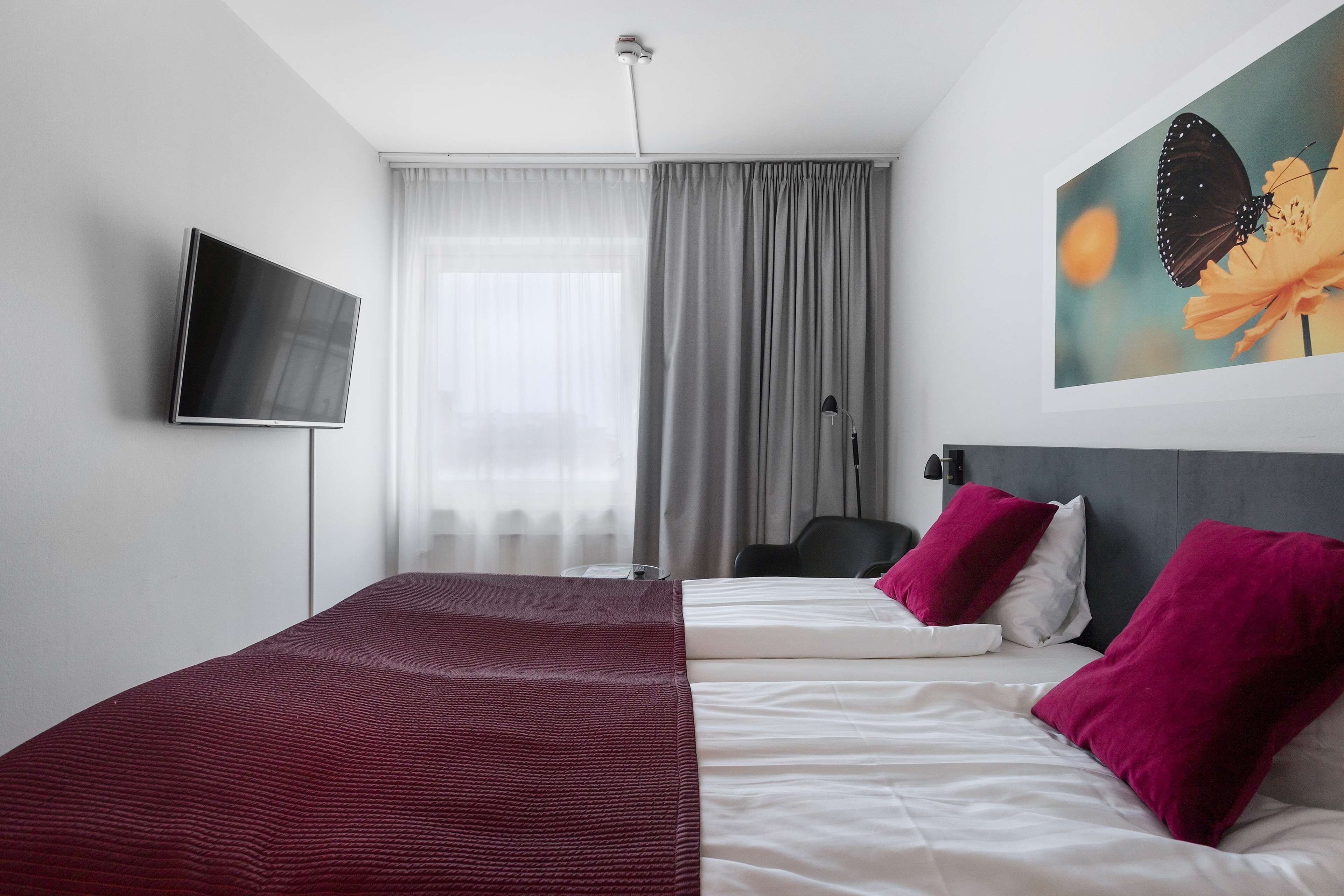 A hotel room with a bed, a flat-screen TV, a painting, and a window with curtains.