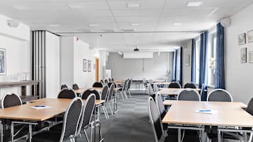A conference room with multiple tables and chairs, white walls, and a projector screen.