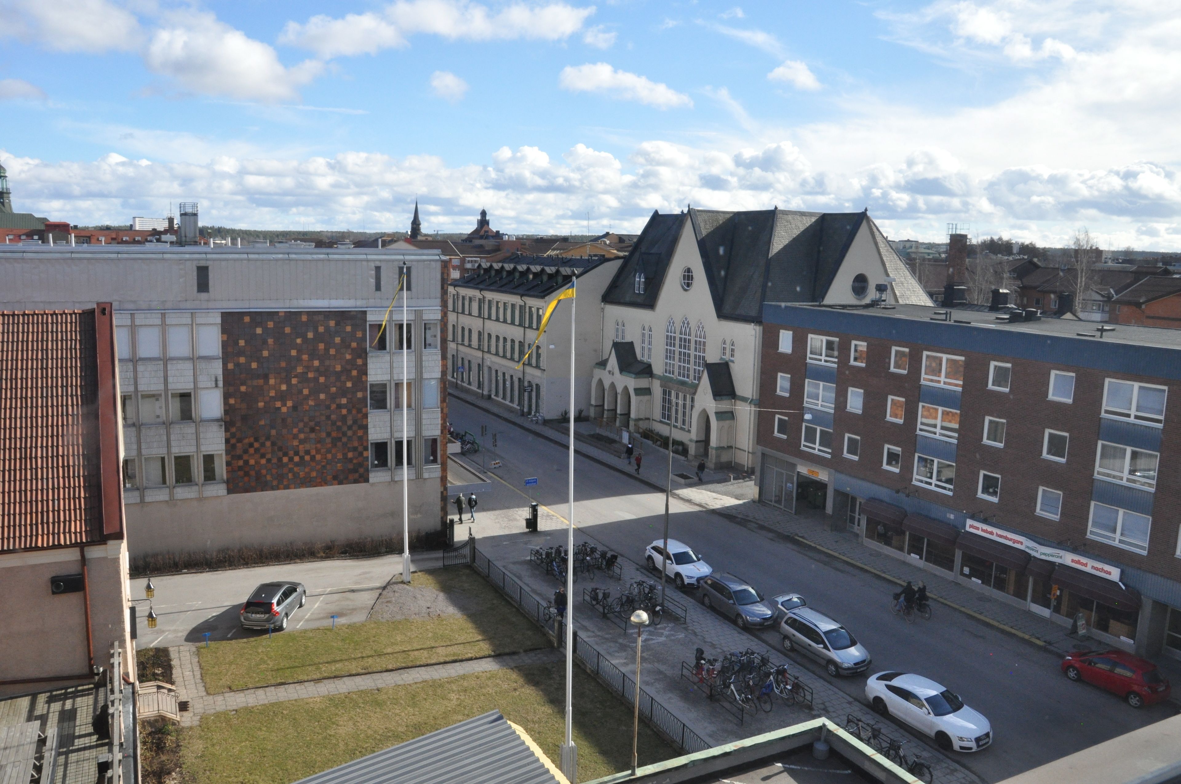 En gatubild med byggnader, bilar och cyklar.