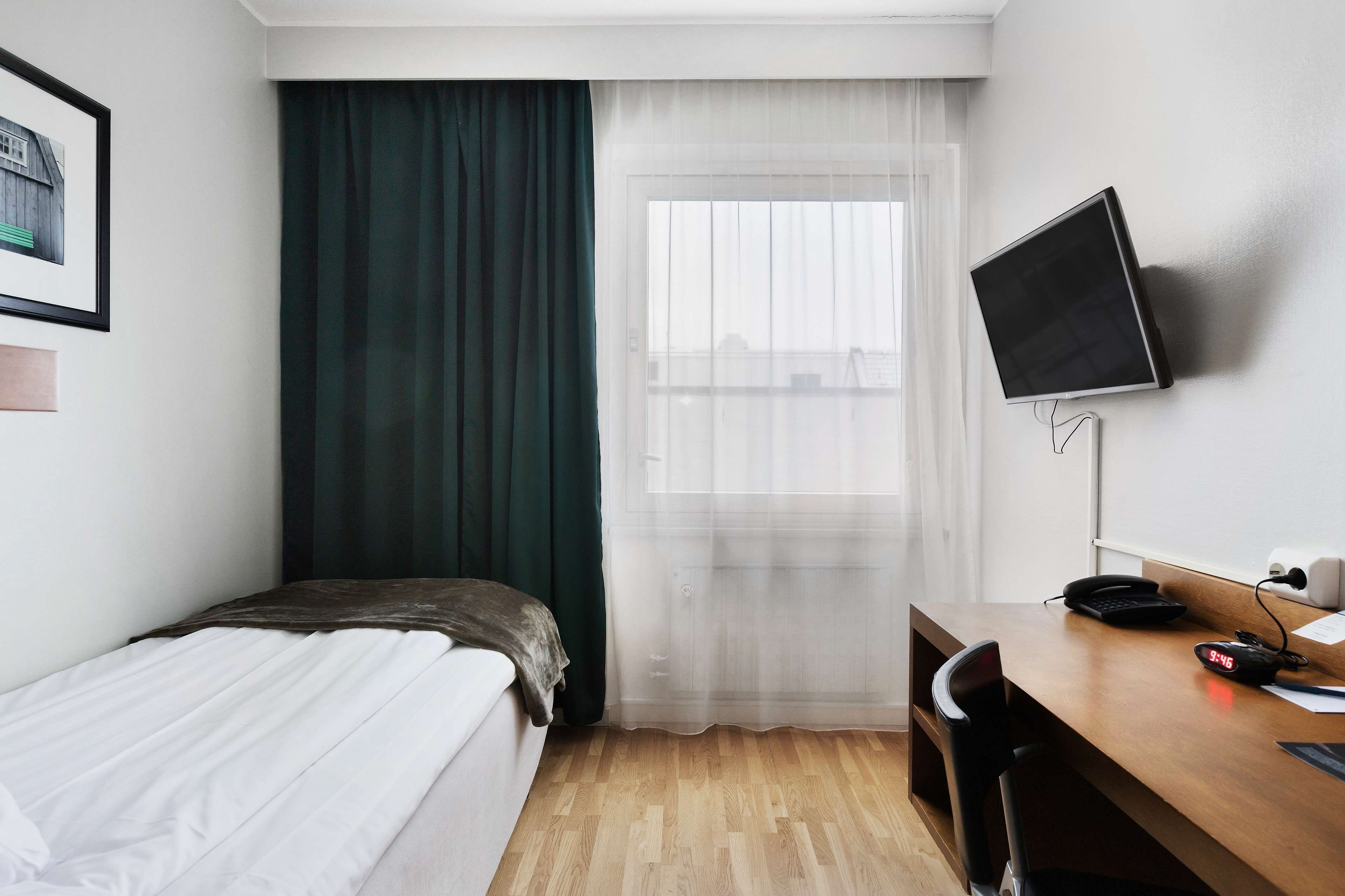 Hotelkamer met een bed, een bureau met computer, een televisie en een raam met gordijnen.