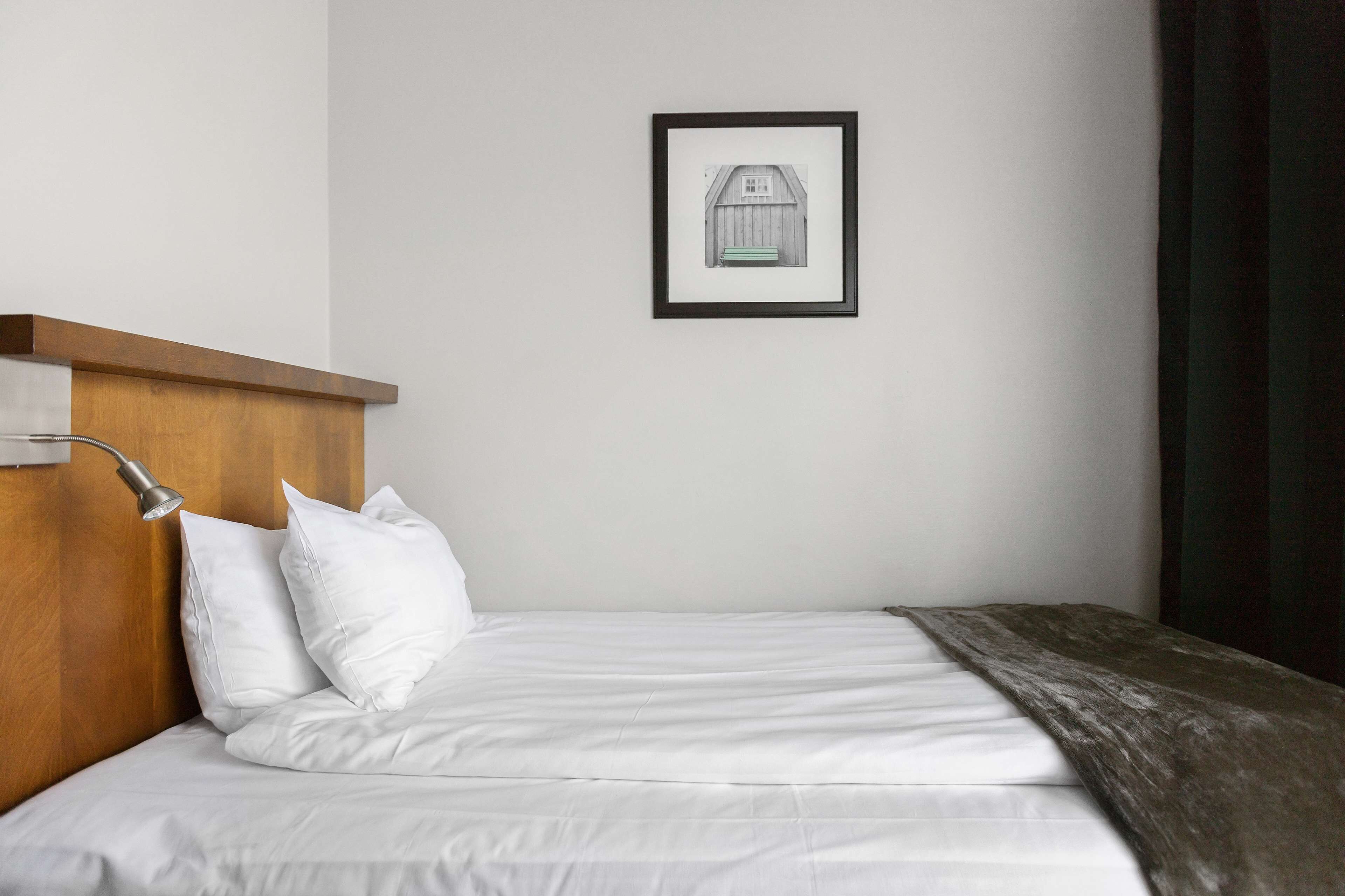 A neatly made bed with white linens, a wooden headboard, and a framed picture on the wall.